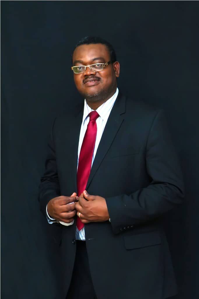Amos Ologunleko in a black suit and red tie